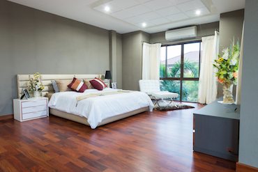 a carpeted room with a high sloping ceiling, two small bright windows, and a two-person bed with a bedside table and lamp on each side